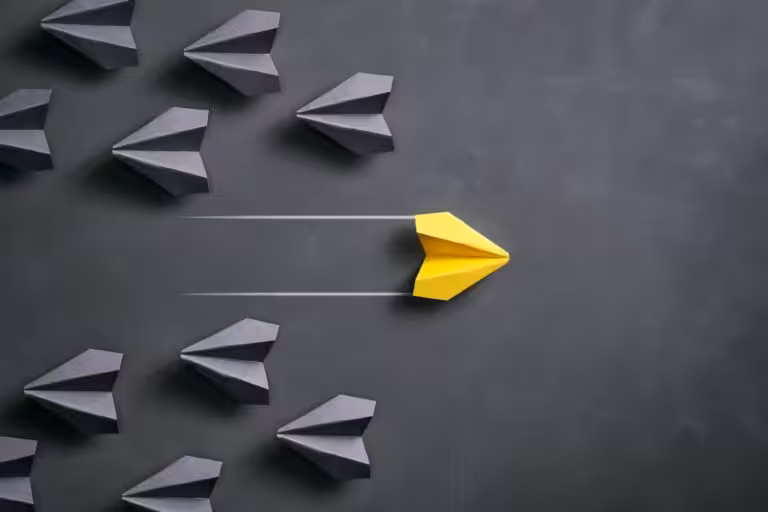 Yellow paper airplane leading black ones on chalkboard.